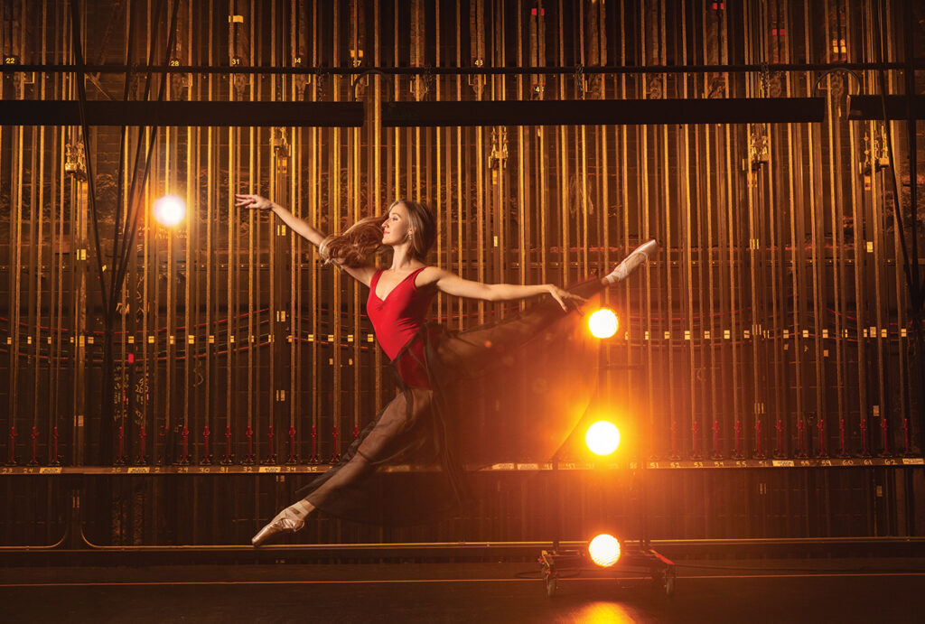 Kara Troester Blythe leaping in a red leotard backstage
