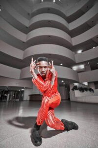 Dancer in a vivid red bodysuit striking an expressive pose inside a sweeping, curved architectural space, creating a dramatic and energetic mood.
