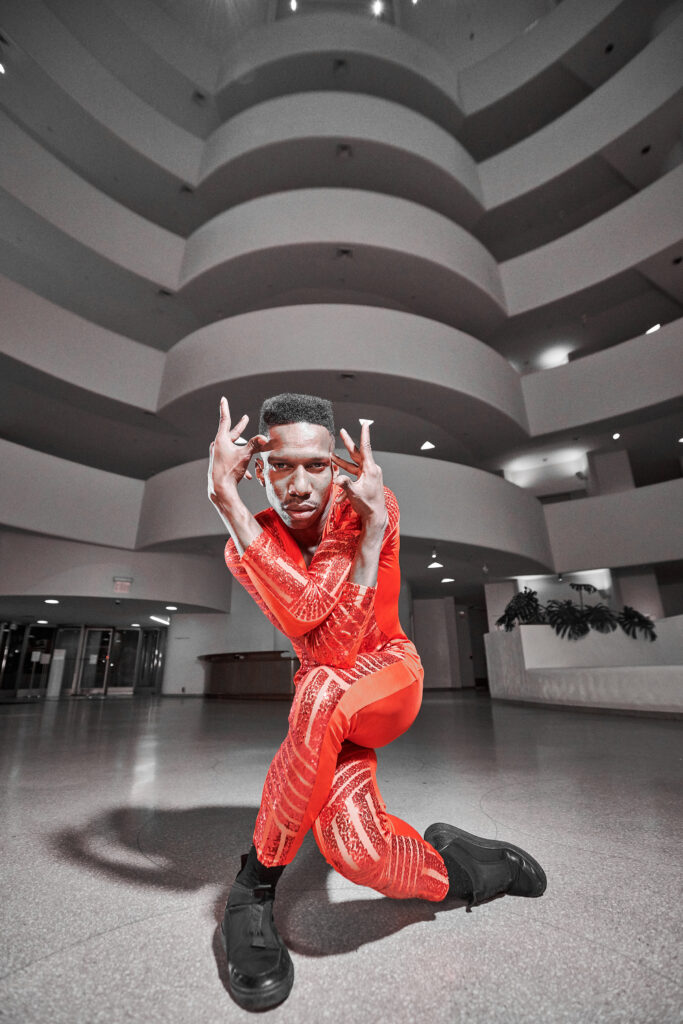 Dancer in a vivid red bodysuit striking an expressive pose inside a sweeping, curved architectural space, creating a dramatic and energetic mood.