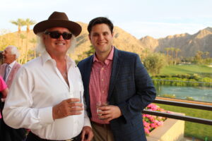 two men pose with cocktails with a view of Palm Springs behind them