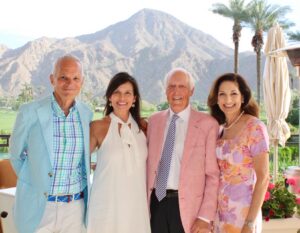 four people pose together for a photo with mountains and palm trees in the background