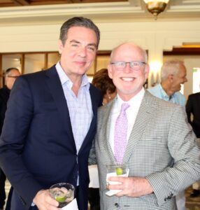 two men in suits pose with cocktails on a patio