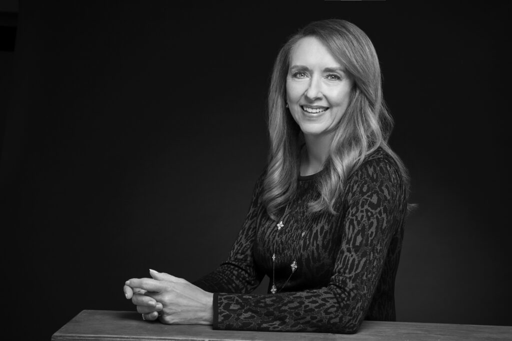 a woman sits for a black and white portrait photograph against a dramatic dark background