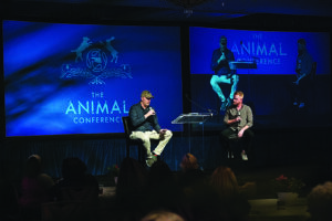 two men join in conversation, speaking into microphones on stage in front of an audience at The Animal Conference
