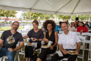 four people sit with a boxed lunch under a tent in an outdoor setting