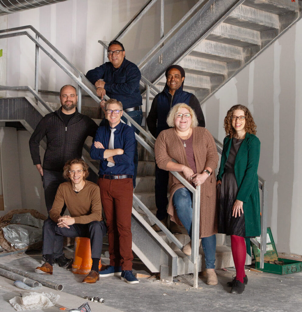 A group of colorfully dressed people pose on a stairwell in an industrial setting