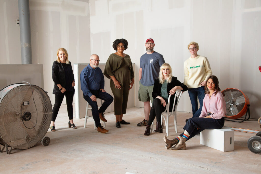 A group of colorfully dressed people pose together in an industrial setting