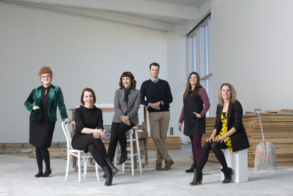 A group of colorfully but professionally dressed people pose together in an industrial setting