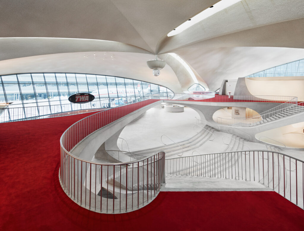 a red carpet and spiraling white corridor and staircase in an airport designed to look like a classic hotel lobby