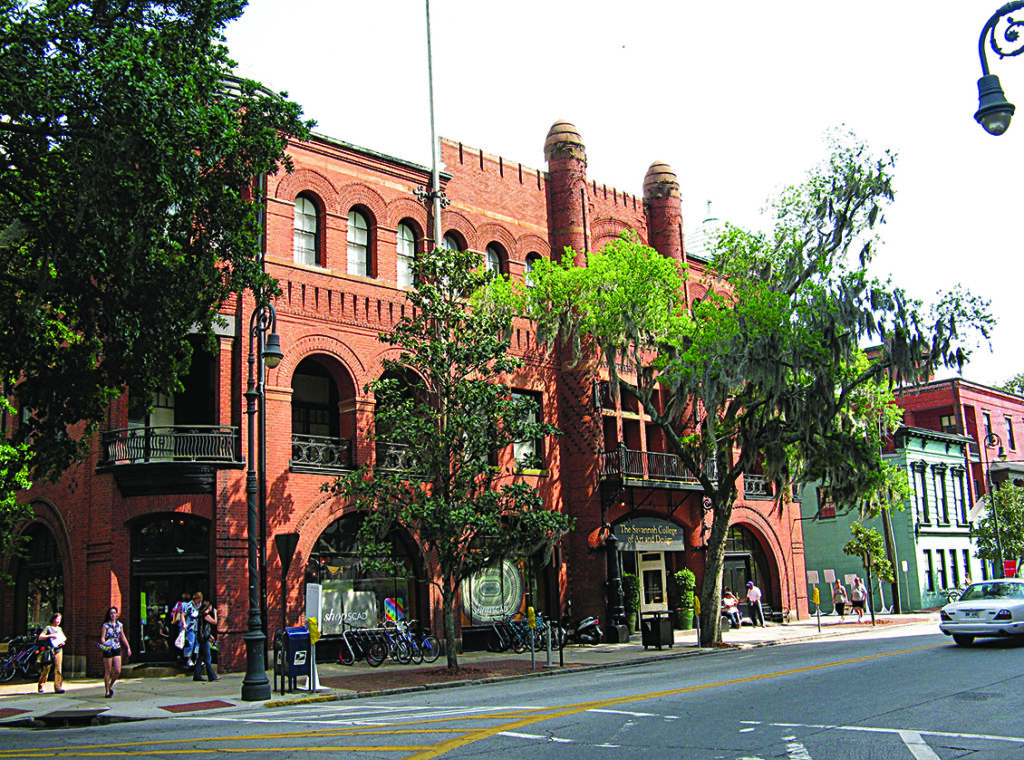 Red brick Savannah College of Art and Design building on a city street with trees, bicycles, and pedestrians.