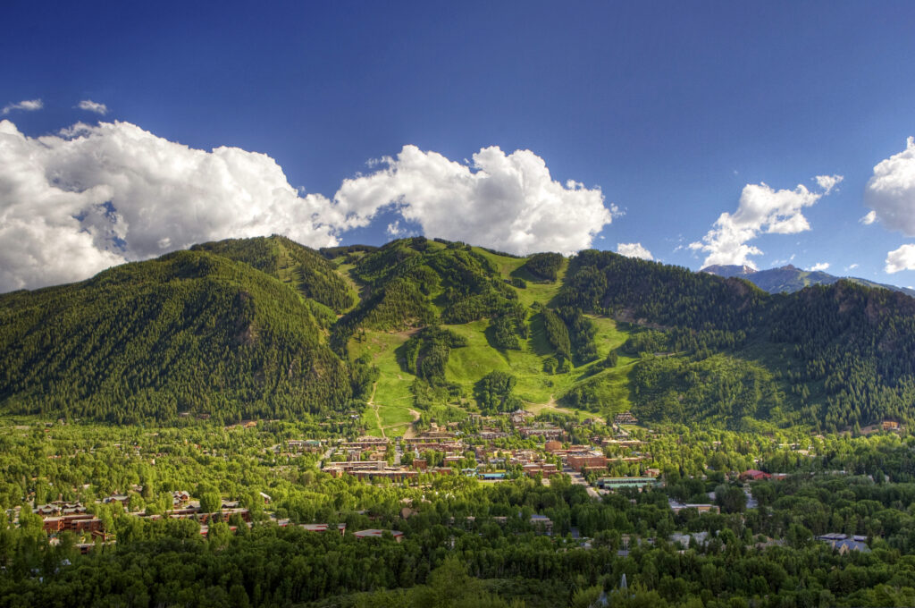 A scenic mountain landscape with the town of Aspen nestled below forested slopes