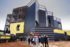 Board Members in hard hats walk into the facade of a building still under construction