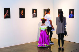 a family enjoys a Celebration of Latino Culture Event by looking at portraits in a gallery with their child who is wearing traditional dress