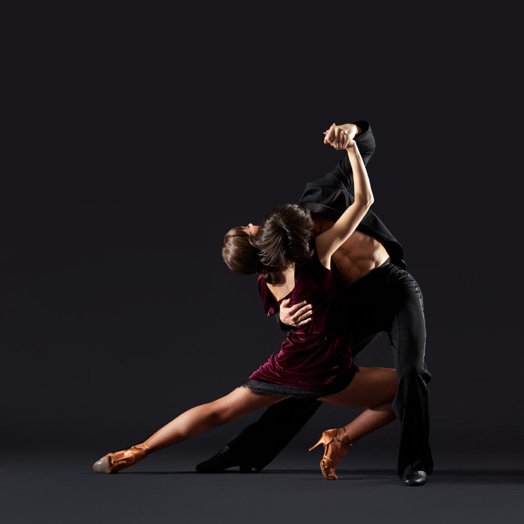Two dancers in a dramatic partnered pose against a dark background