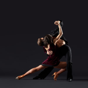 Two dancers in a dramatic partnered pose against a dark background