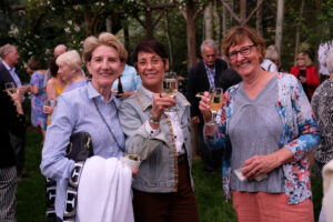 A small group of people standing together at an outdoor art festival, smiling and holding glasses of white wine