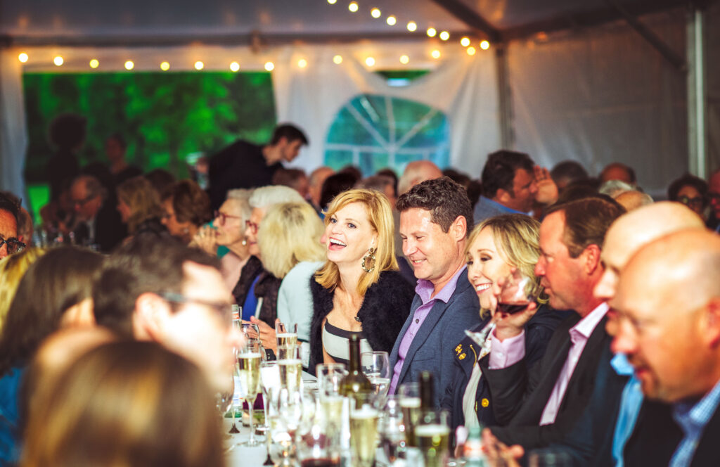 a group of people enjoy a dinner fundraiser under a canopy tent
