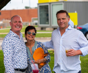 three people pose together in summer attire at an outdoor event