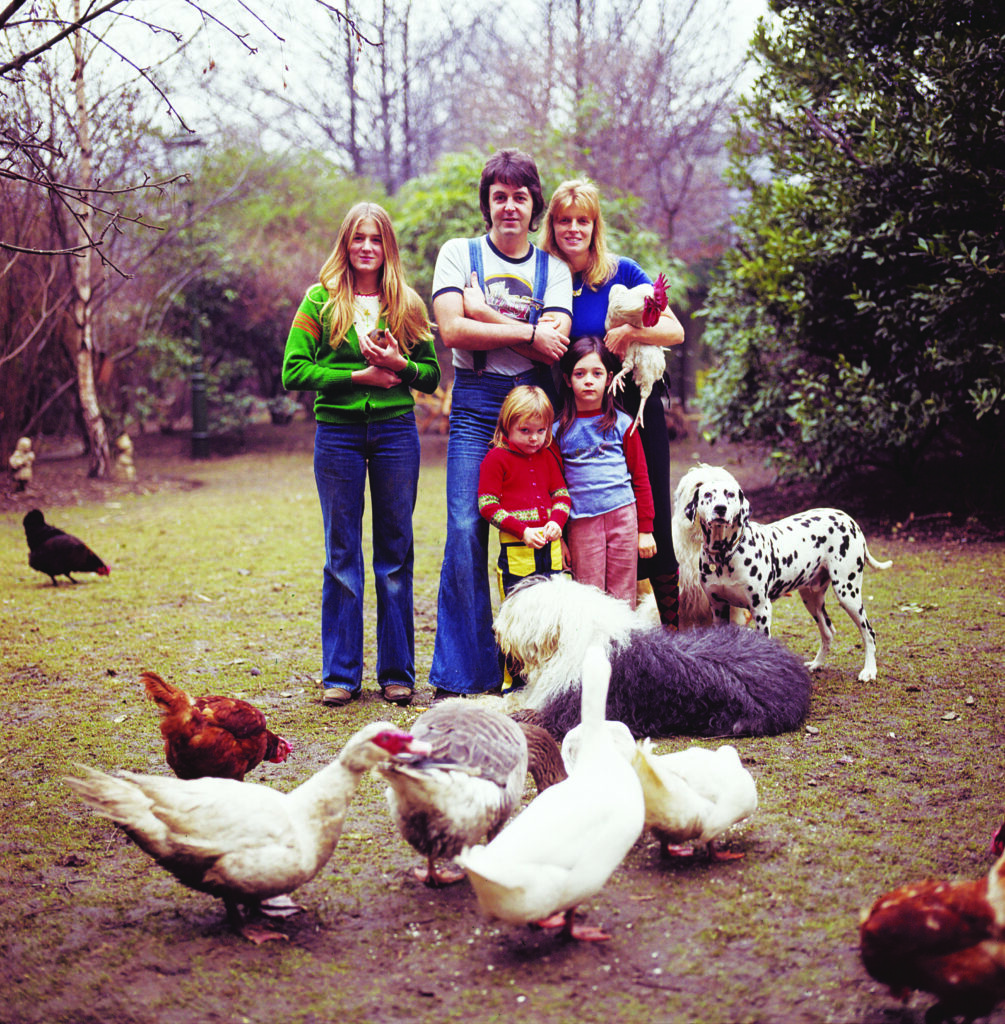 A family stands together in an outdoor setting, surrounded by dogs and chickens
