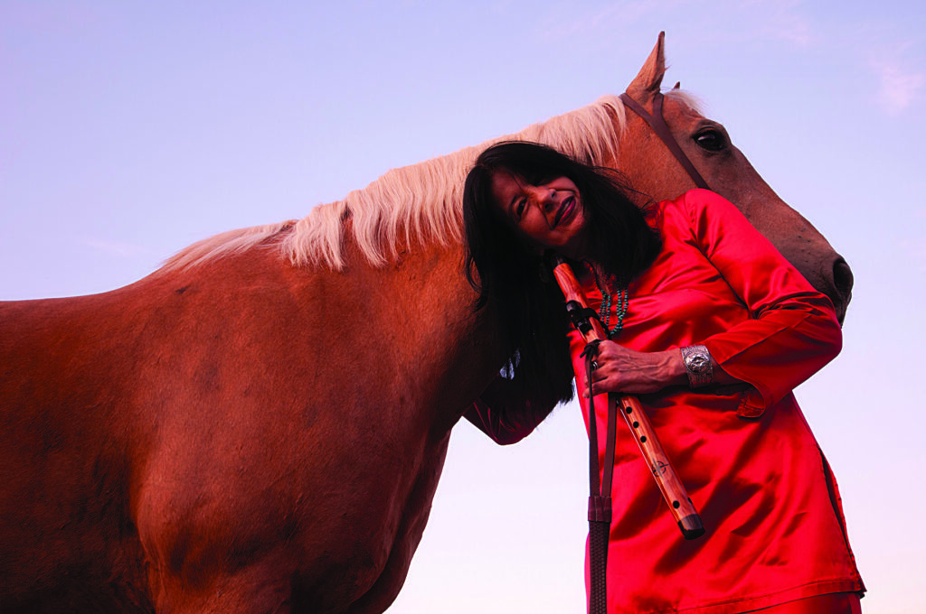 a woman in red leans against a horse and hugs the horse's neck