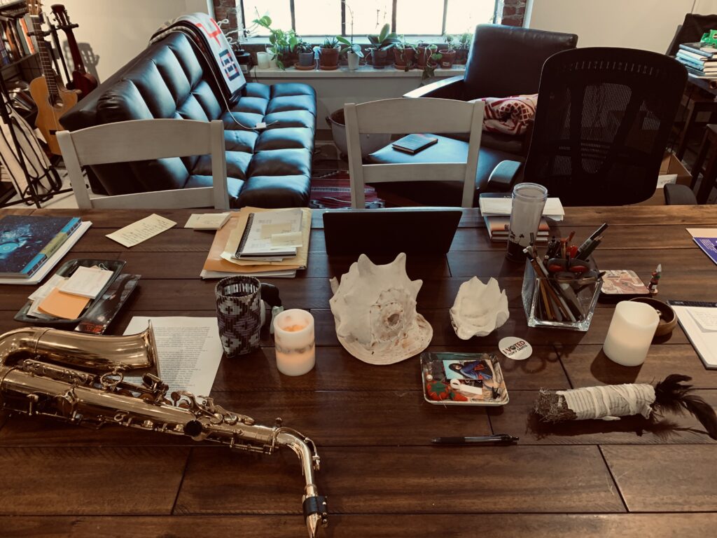 A creative workspace with musical instruments, writing materials, and personal objects arranged on a large wooden table, supporting the surrounding content by illustrating a setting of artistic and intellectual activity.