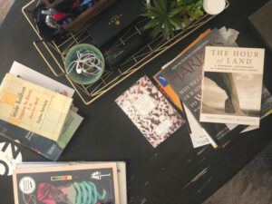 A coffee tabletop scattered with books, magazines, and small desk items.