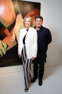 a couple stands together in front of a large painted canvas