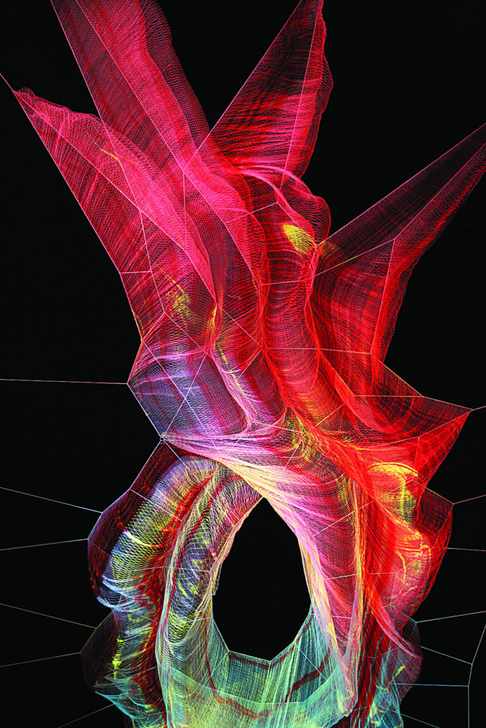 Illuminated red, pink, and white woven net sculpture suspended on cables against a black background, forming twisting, layered shapes with visible mesh texture.