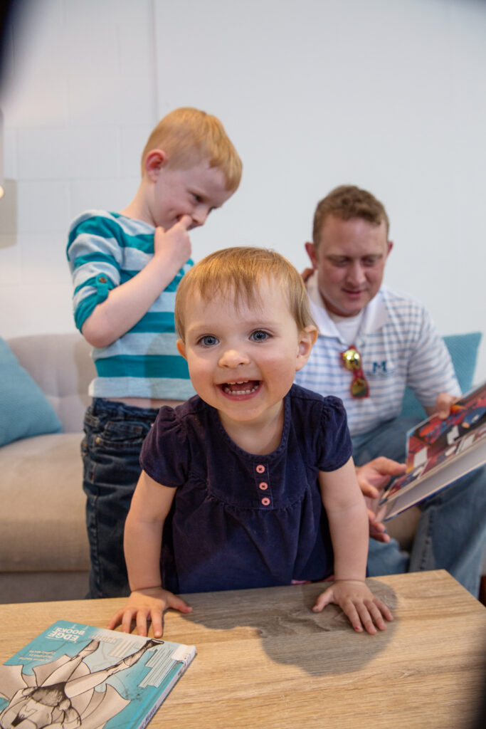 a toddler leans across a coffee table as its family engages in art activities in the background