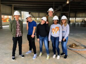 a group of teenagers and their adult advisor wear hardhats to visit a construction site