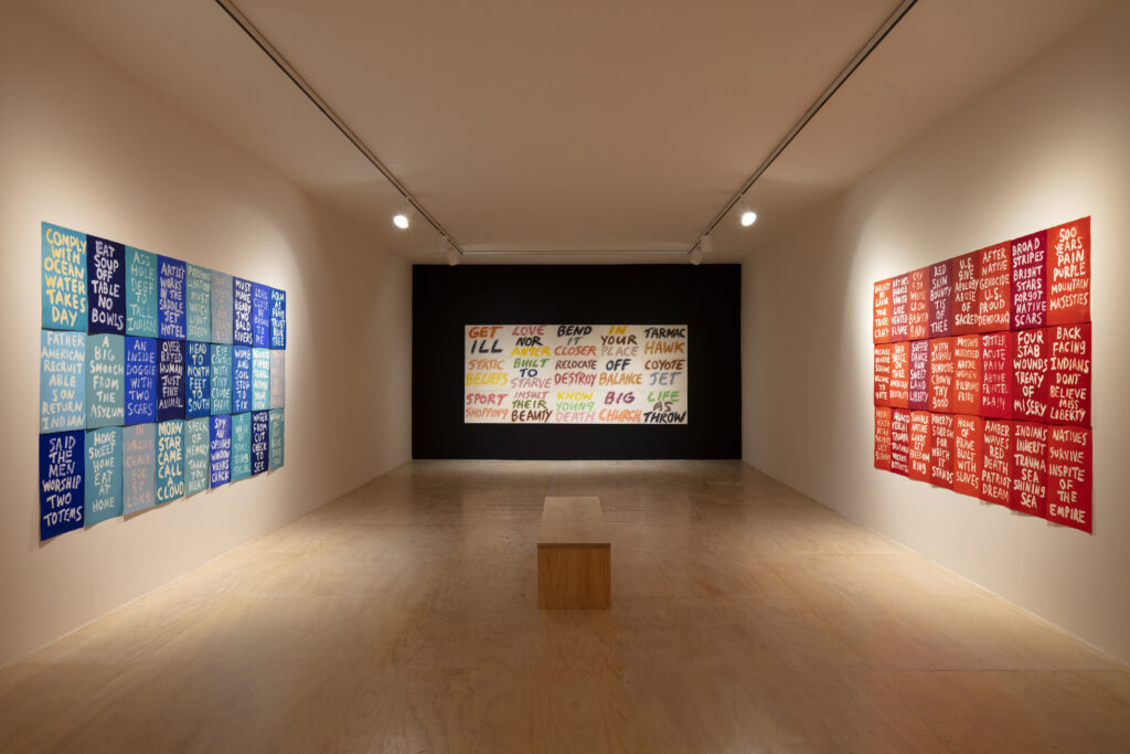 a modern art gallery with a blue patchwork of protest word art on the left, red patchwork of protest word art on the right, and a white patchwork of protest word art on the back wall