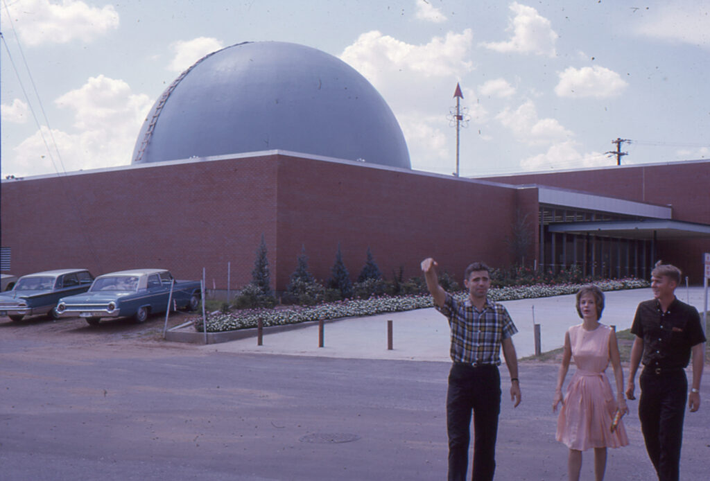 people wave in front of a brick building with a domed roof