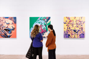 two women look at a painting on a gallery wall