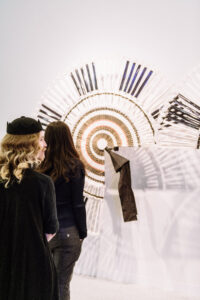 people walk past a sculptural piece in a bright gallery space