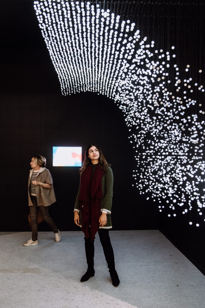 A woman looks up at a light sculpture in dark gallery