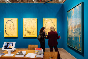 three women look at artworks on a gallery with a blue wall