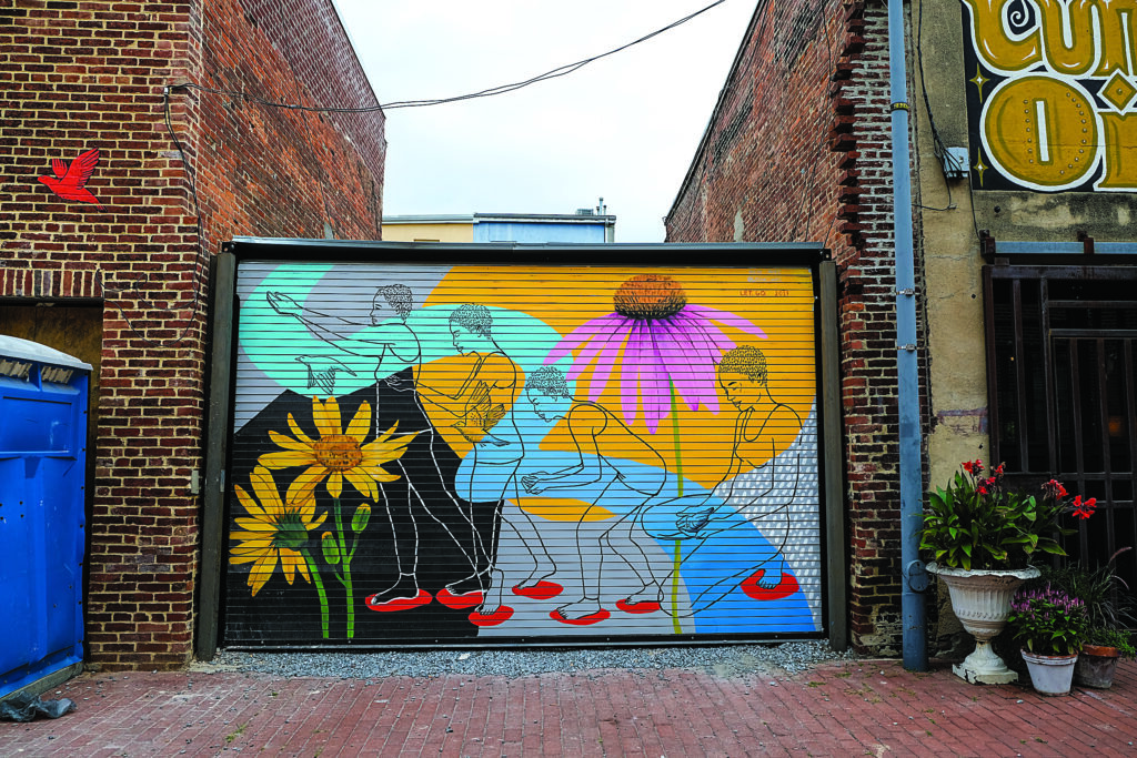 A colorful mural on a garage door featuring outlined human figures and large flowers