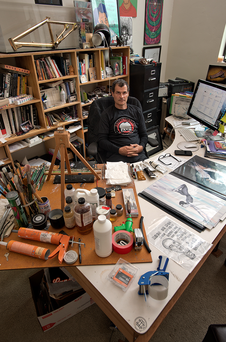 A man sits behind a desk in front of a bookshelf