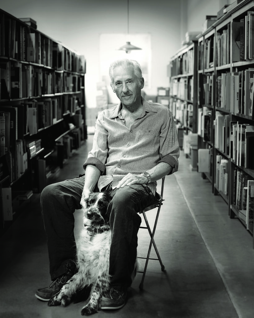 a man sits in a library aisle and pets a dog sitting between his legs