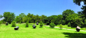 A grassy lake park dotted with large dark geometric sculptures