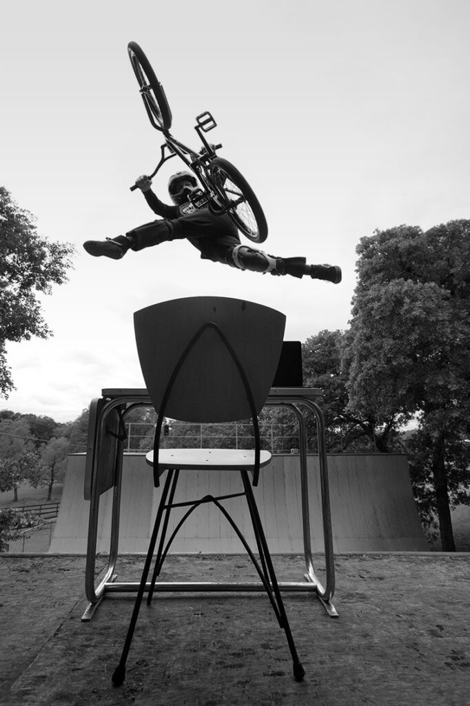 A man on a bicycle jumps through the air over a desk in a skate park
