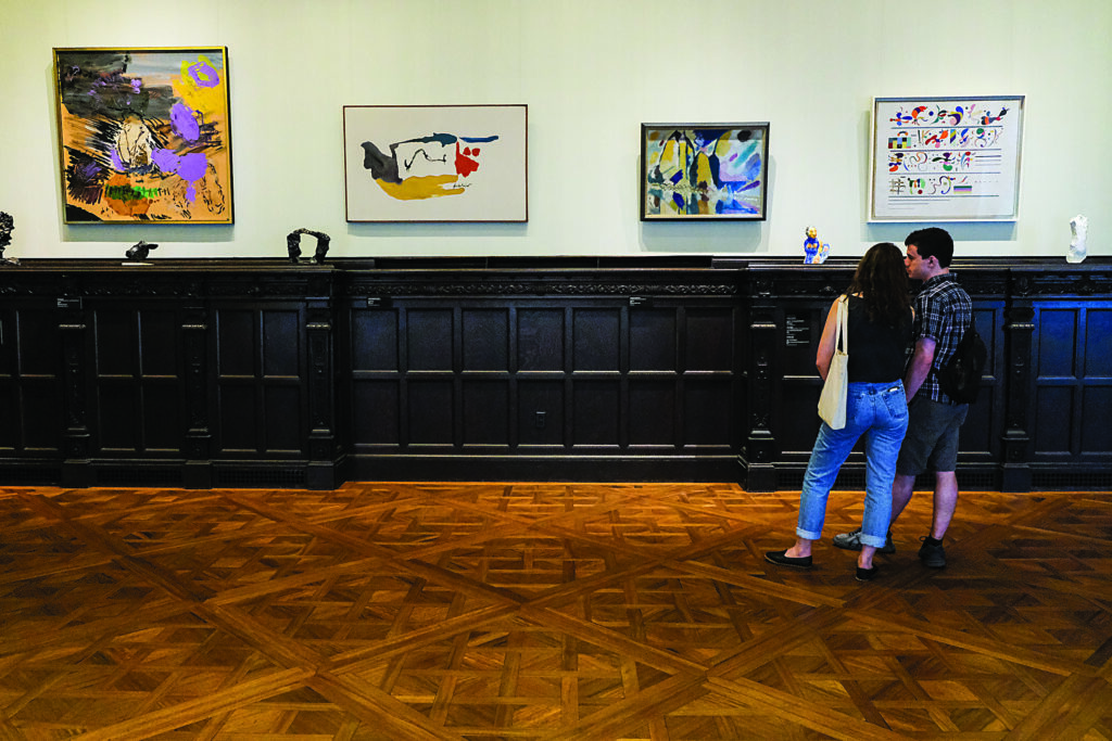 two people observe art on a traditional gallery wall