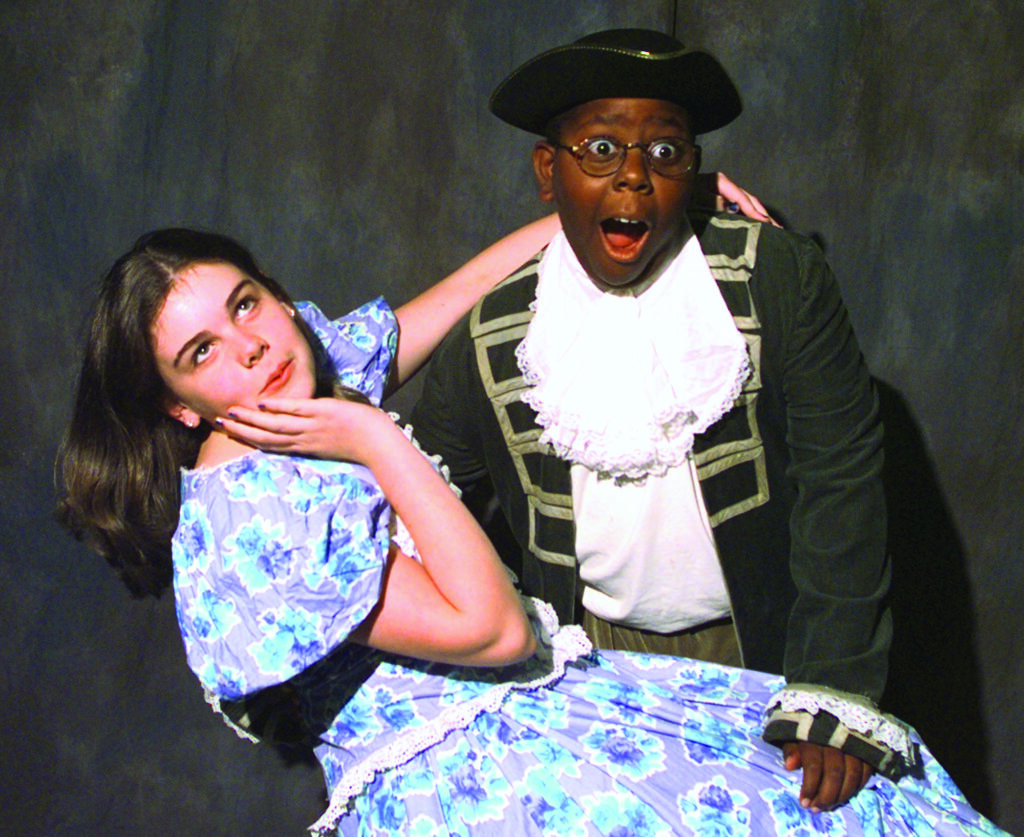 two young actors play a scene where a girl in a blue dress swoon in the arms of a boy dressed as a captain