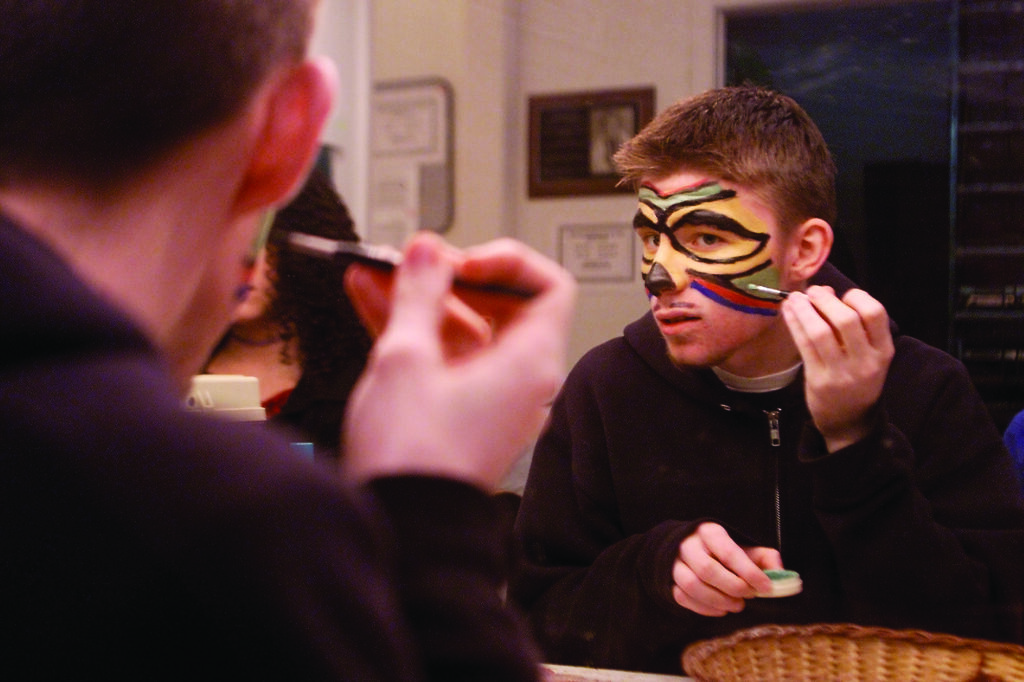 a student in an advanced theater class arts class carefully applies stage makeup in a mirror