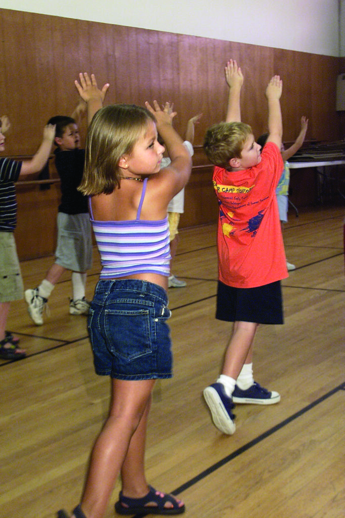 children sway to one side with their arms raised as they practice together