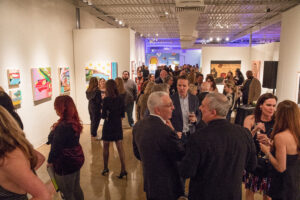 a crowd of people walk through an art gallery corridor