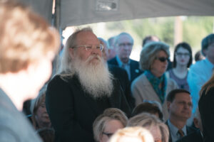 a man smiles from the crowd as he listens engaged with a speaker at a groundbreaking