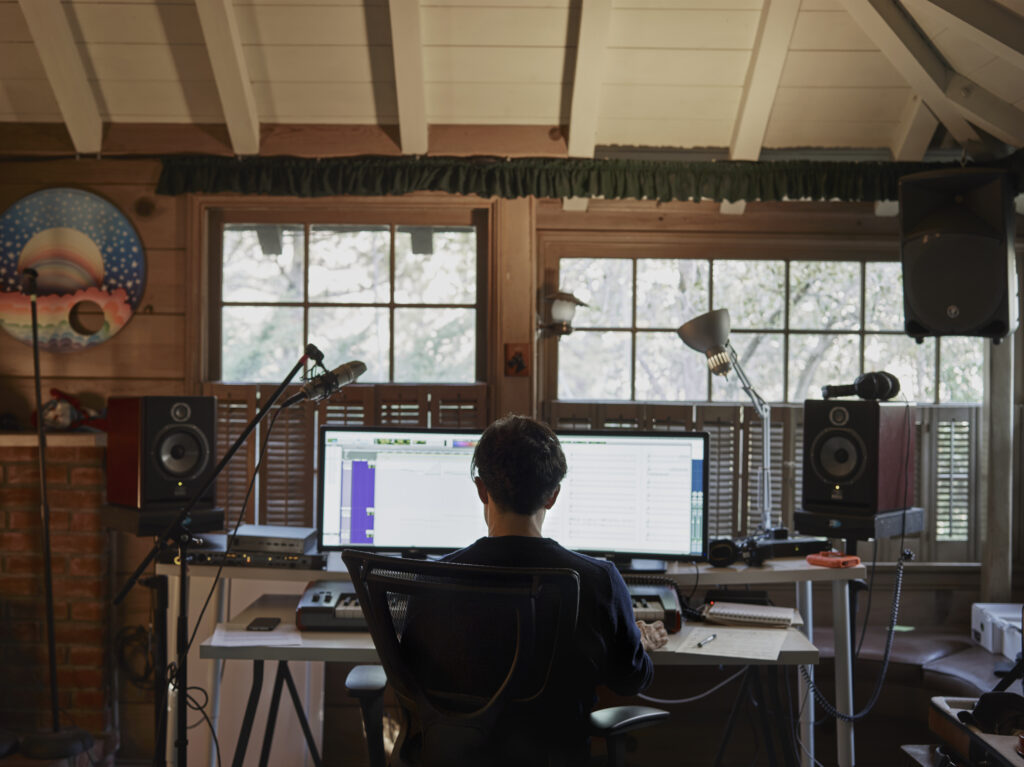 a man faces an oversized computer screen on a desk in front of a window