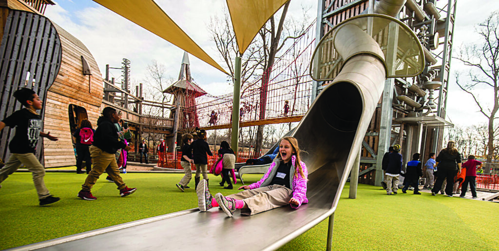 children explore a new playground as a girl is thrilled to take a turn down a new slide