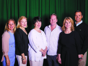 a group of people pose in front of a green curtain